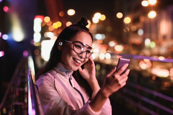 laimīga aziātu meitene, kam ir video tērzēšana, izmantojot viedtālruni un austiņās